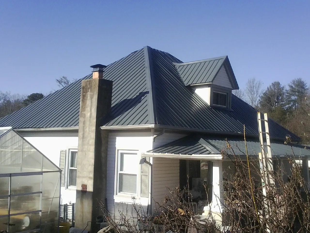 Dark blue standing seam metal roof on a white farmhouse with dormer — Slate & Tile Roof Repair by Roofing Brothers in East Syracuse