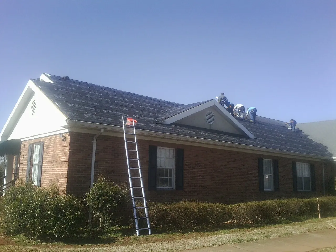 Crew tearing shingles off a brick ranch roof with a ladder set — Emergency Roof Repair work by our crew in East Syracuse