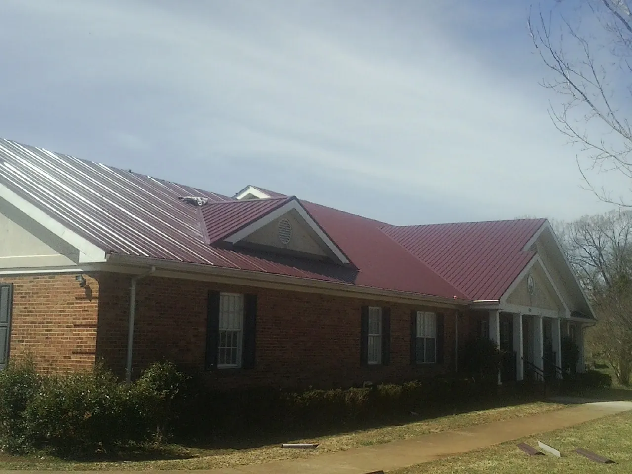 Red metal roof with gabled entries on a long brick building, from a Hail Damage Roof Repair job in East Syracuse