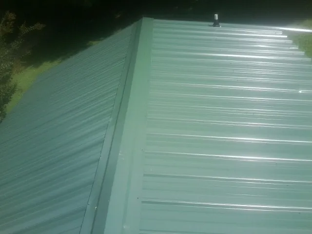 New green metal panels meeting at the ridge of a roof — Flat Roof Repair work by our crew in East Syracuse