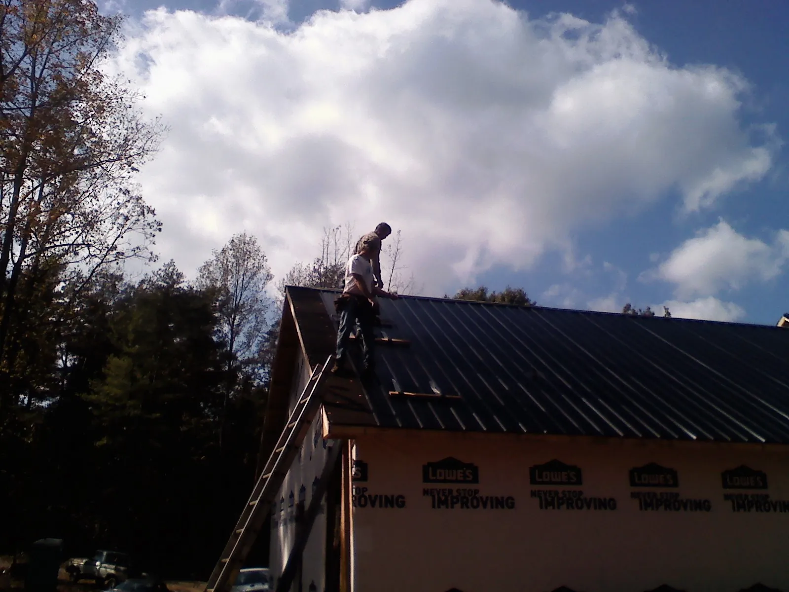 Roofer fastening dark metal panels high against a cloudy sky, from a Roof Inspection job in East Syracuse