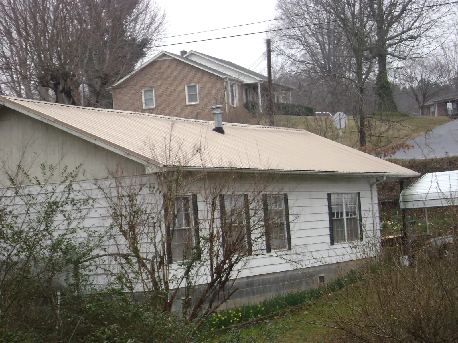 Tan metal roof on a white sided house set into a hillside — Commercial Roofing by Roofing Brothers in East Syracuse