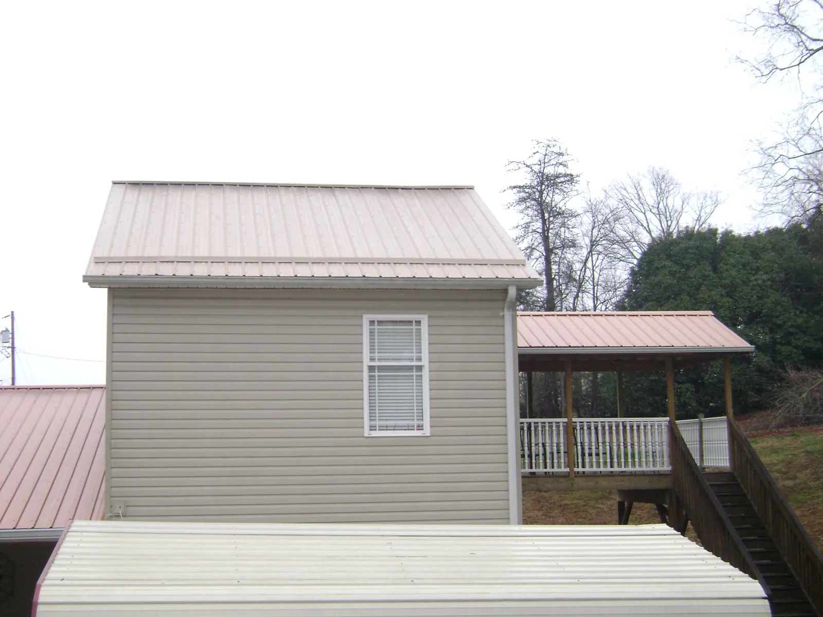 Tan metal roofs on a two story addition and attached porch, from a Roof Replacement job in East Syracuse