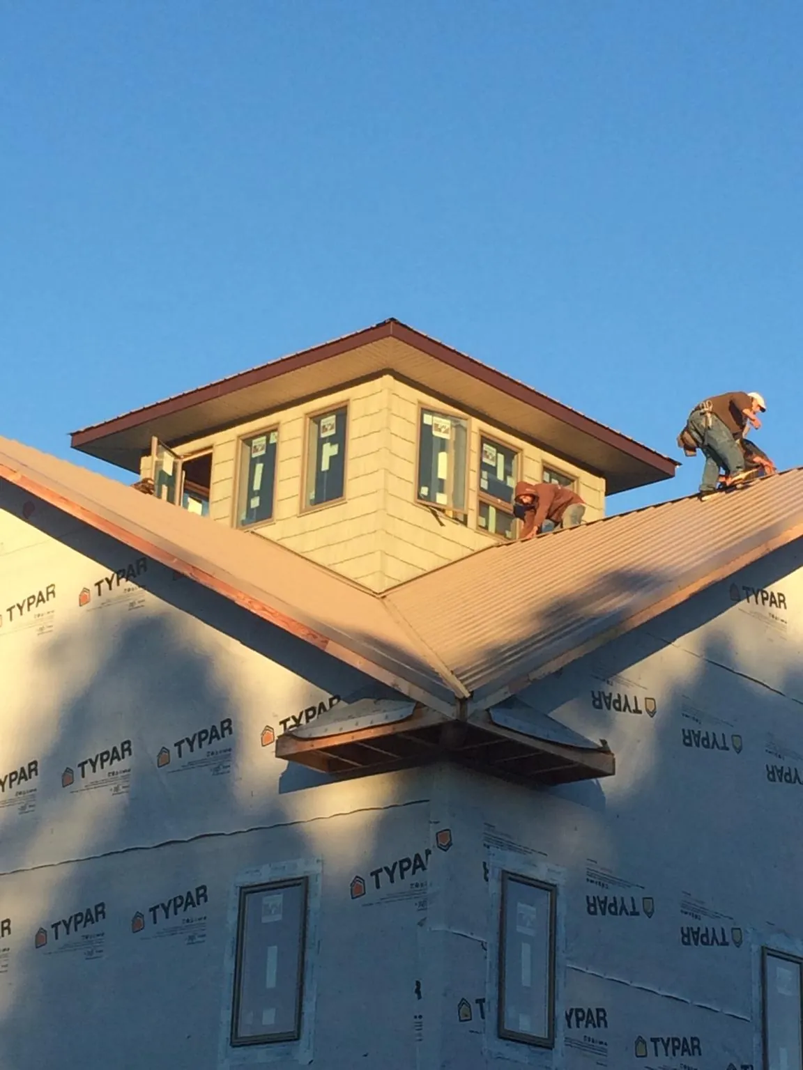 Roofers working around a rooftop cupola on a new metal roof at sunset in East Syracuse